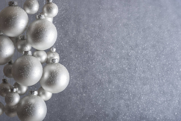 Matt színű ezüst karácsonyi labdák lóg, egy szürke háttér, miközben havazik, szelektív összpontosít, a karácsonyi banner vagy üdvözlőkártya. - Fotó, kép