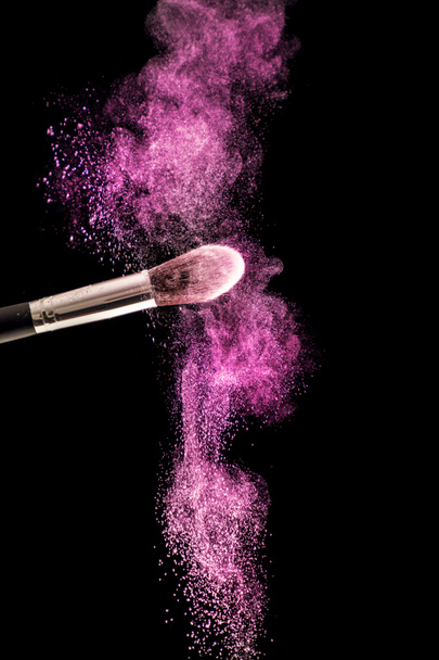 Make up brush with purple dust powder explosion isolated on black background. Beauty and fashion concept. Close up, selective focus - Photo, Image