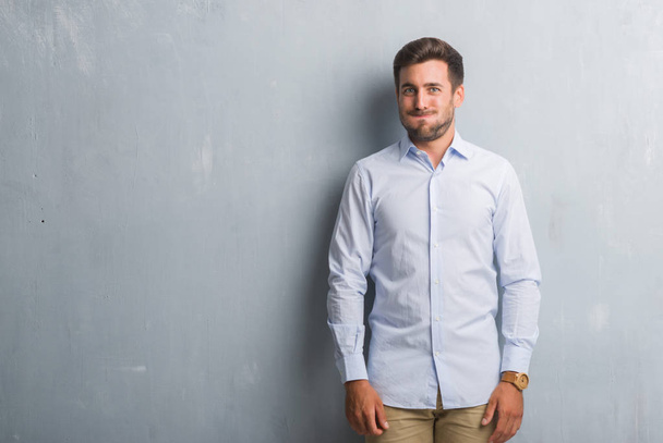 Handsome young business man over grey grunge wall wearing elegant shirt puffing cheeks with funny face. Mouth inflated with air, crazy expression. - Фото, изображение