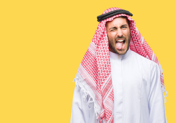 Jovem homem bonito vestindo keffiyeh sobre fundo isolado furar a língua para fora feliz com expressão engraçada. Conceito de emoção
. - Foto, Imagem