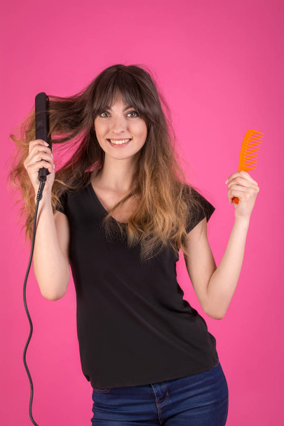 Woman with a hair curler and a comb. Girl with disheveled hair on a pink - Photo, Image
