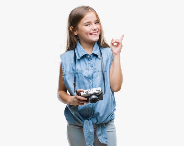 Menina bonita jovem tirar fotos usando a câmera vintage sobre fundo isolado muito feliz apontando com a mão e o dedo para o lado
 - Foto, Imagem