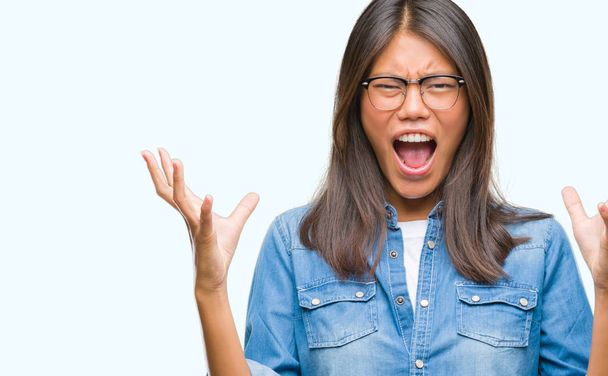 若いアジア女性にメガネをかけて背景クレイジーを分離し、怒って叫んで、叫んで積極的な表現と腕を上げます。欲求不満のコンセプト. - 写真・画像