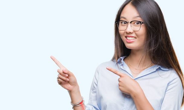 Jeune femme d'affaires asiatique portant des lunettes sur fond isolé souriant et regardant la caméra pointant avec deux mains et doigts sur le côté
. - Photo, image