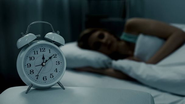Young lady resting in her bed, midnight time shown on alarm clock, night dreams - Фото, зображення