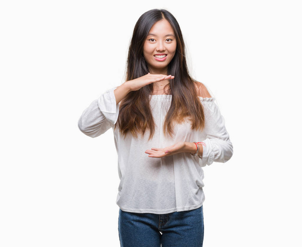 junge asiatische Frau über isoliertem Hintergrund gestikulierend mit Händen, die große und große Zeichen zeigen, Maßsymbol. Lächelnd in die Kamera blickend. Messkonzept. - Foto, Bild
