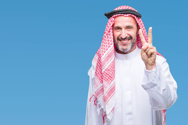 シニアのアラブ人にクーフィーヤを着て分離を示す背景と指で上向き数は自信を持って、幸せな笑顔 2. - 写真・画像