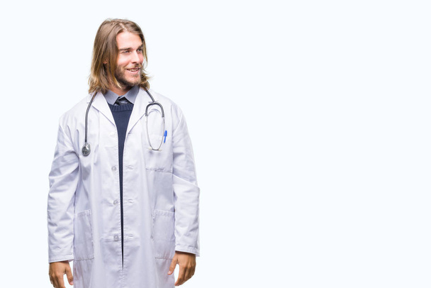 Young handsome doctor man with long hair over isolated background looking away to side with smile on face, natural expression. Laughing confident. - Fotó, kép