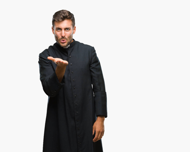 Young catholic christian priest man over isolated background looking at the camera blowing a kiss with hand on air being lovely and sexy. Love expression. - 写真・画像