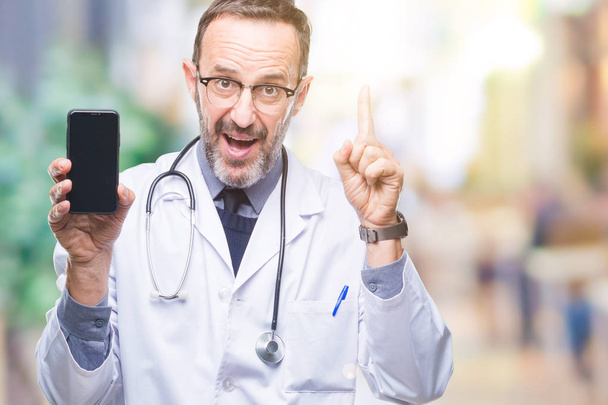 Medico anziano di mezza età hoary mostrando schermo smartphone su sfondo isolato sorpreso con un'idea o una domanda che punta il dito con la faccia felice, numero uno
 - Foto, immagini