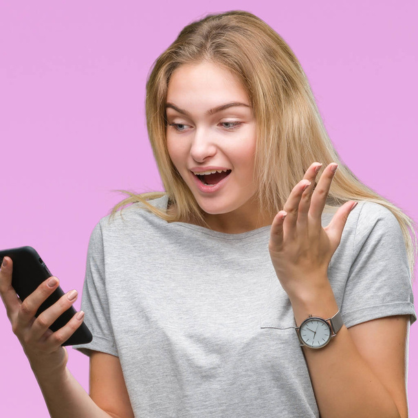 Young caucasian woman sending message using smartphone over isolated background very happy and excited, winner expression celebrating victory screaming with big smile and raised hands - Foto, immagini