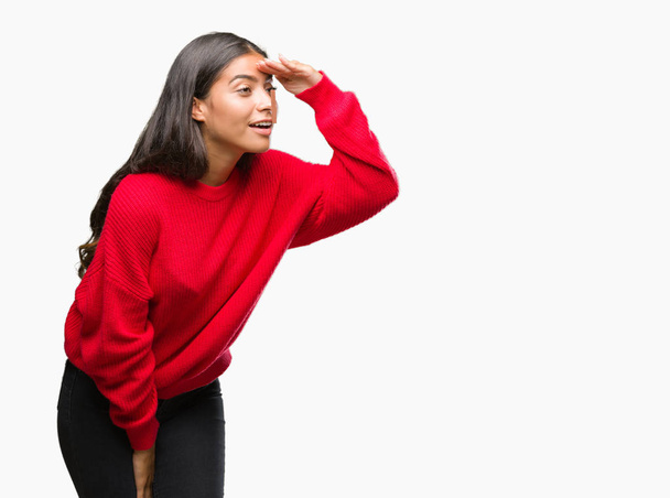 Young beautiful arab woman wearing winter sweater over isolated background very happy and smiling looking far away with hand over head. Searching concept. - Fotoğraf, Görsel