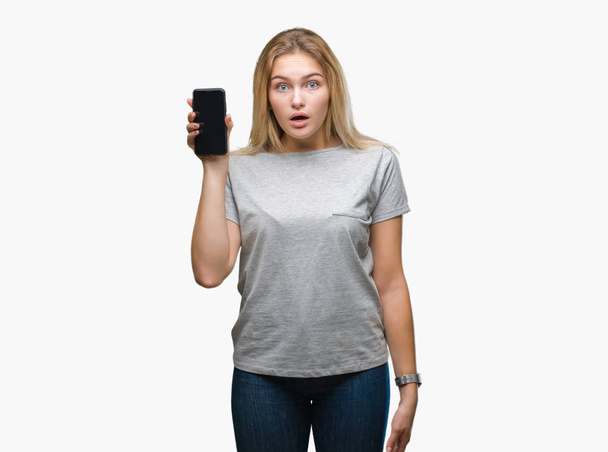 Young caucasian woman showing screen of smartphone over isolated background scared in shock with a surprise face, afraid and excited with fear expression - Фото, изображение