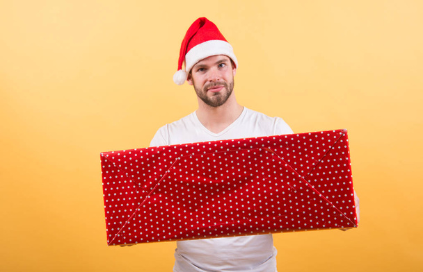 man in santa hat hold christmas present. The morning before Xmas. delivery christmas gifts. man enjoy the holiday. Christmas composition. Merry Christmas and Happy Holidays. Colorful fun - Фото, изображение