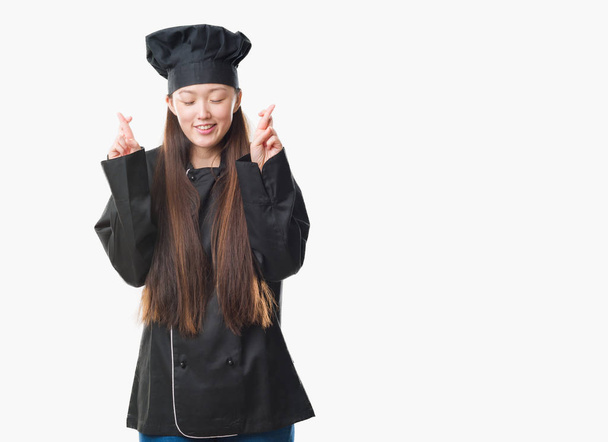 Giovane donna cinese su sfondo isolato indossando uniforme chef sorridente incrociando le dita con speranza e gli occhi chiusi. Fortuna e concetto superstizioso
. - Foto, immagini