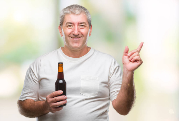 Guapo hombre mayor bebiendo botella de cerveza sobre fondo aislado muy feliz señalando con la mano y el dedo a un lado
 - Foto, imagen