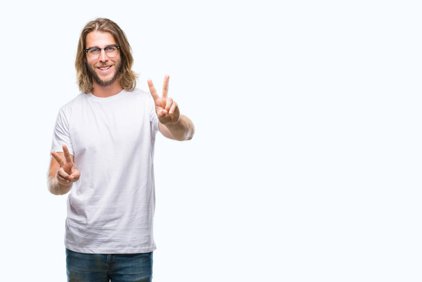 Young handsome man with long hair wearing glasses over isolated background smiling looking to the camera showing fingers doing victory sign. Number two. - Photo, Image