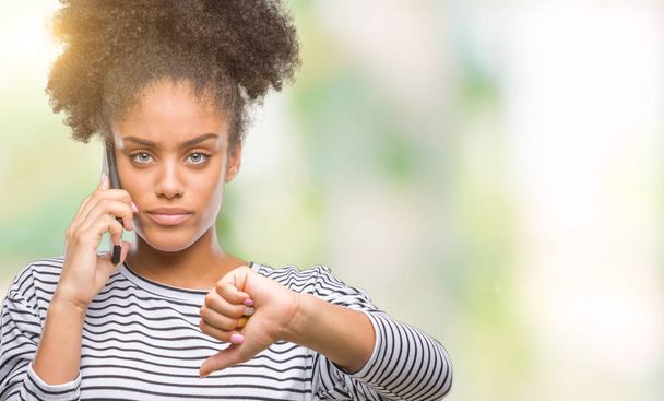 Jeune femme afro-américaine parlant au téléphone sur fond isolé avec le visage en colère, signe négatif montrant aversion avec les pouces vers le bas, concept de rejet
 - Photo, image