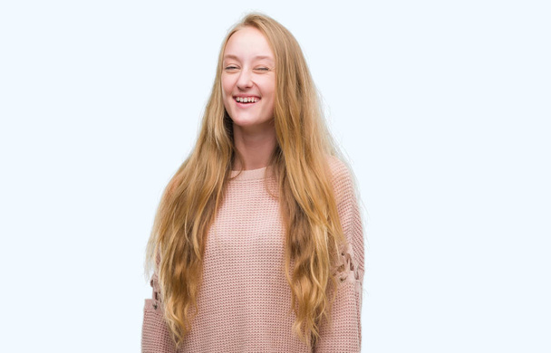 Rubia adolescente mujer vistiendo suéter rosa guiño mirando a la cámara con expresión sexy, cara alegre y feliz
. - Foto, Imagen