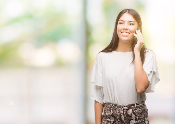 Young beautiful hispanic using smartphone with a happy face standing and smiling with a confident smile showing teeth - Photo, Image
