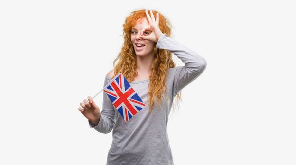 指の間から見て目に手で ok サインをして笑っている幸せそうな顔でイギリスの旗を保持している赤毛の若い女性 - 写真・画像