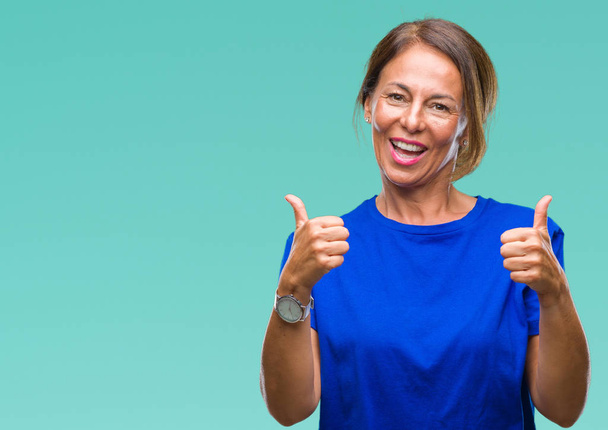 Middle age senior hispanic woman over isolated background success sign doing positive gesture with hand, thumbs up smiling and happy. Looking at the camera with cheerful expression, winner gesture. - Photo, image