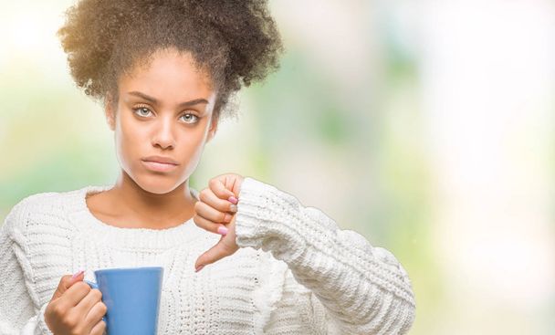 Young afro american woman driking cup of coffee over isolated background with angry face, negative sign showing dislike with thumbs down, rejection concept - Фото, зображення