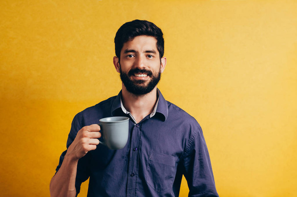 Portrait of handsome man drinking coffee over yellow background - Zdjęcie, obraz