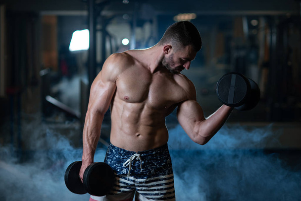 Handsome young muscular man exercising with dumbbells. Guy trains his bicep - Foto, immagini