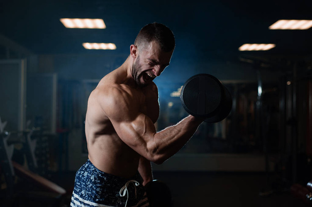 Handsome young muscular man exercising with dumbbells. Guy trains his bicep - Foto, Imagem