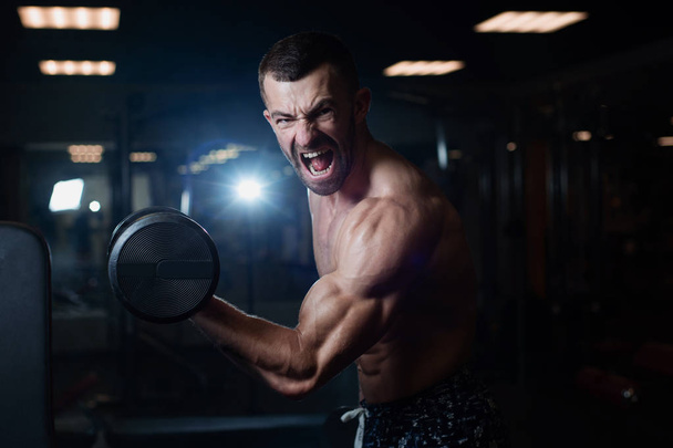 Handsome young muscular man exercising with dumbbells. Guy trains his bicep - Fotografie, Obrázek