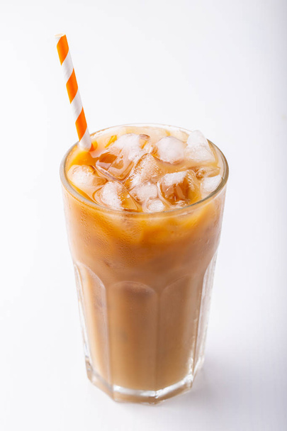 Ice coffee in a tall glass with cream poured over and coffee beans. Cold summer drink on white background. - Photo, image