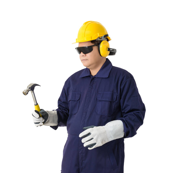 Portret van een werknemer in Mechanic Jumpsuit houdt een hamer met helm oorkappen, beschermende handschoenen en veiligheidsbril geïsoleerd op een witte achtergrond uitknippad - Foto, afbeelding