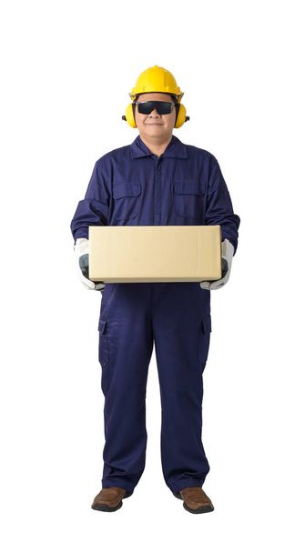Portret van een werknemer in Mechanic Jumpsuit met helm oorkappen, beschermende handschoenen en veiligheidsbril droeg een doos geïsoleerd op een witte achtergrond uitknippad - Foto, afbeelding