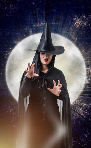 Álló nő fekete ijesztő boszorkány halloween jelmez, magic lámpák és nagy Hold Halloween art design háttérrel - Fotó, kép