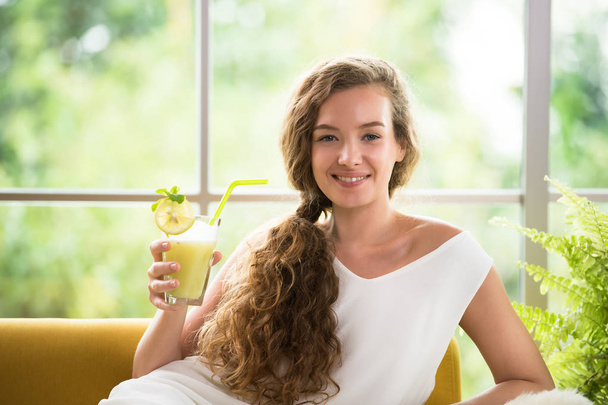 gesunde junge Frau, die auf einer Couch liegt und ein Glas Fruchtsaft in der Hand hält und entspannt und bequem aussieht - Foto, Bild