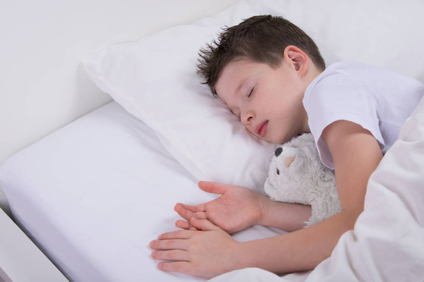 the boy is sleeping with his favorite toy, in a white bed - Foto, Imagen