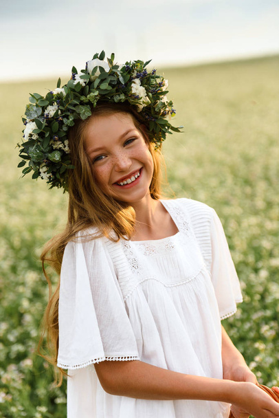 Girl in white dress and wreath from wild flowers  - Фото, зображення