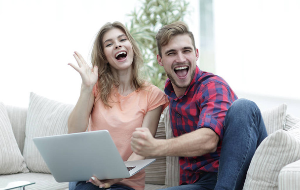 young couple rejoices,sitting on the couch in front of the open laptop - Foto, afbeelding