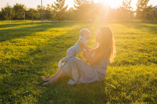 junge Frau mit Junge auf der Wiese an einem sonnigen Tag. glückliche Familie im Sommersonnenuntergang. Mutter mit Baby. - Foto, Bild