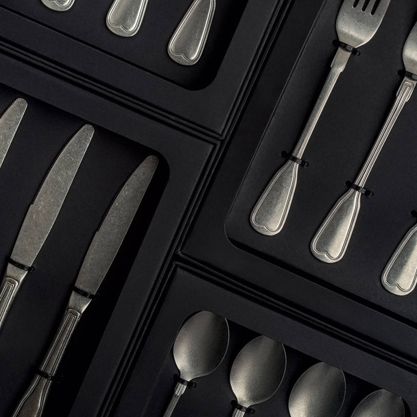 Top view of silver collection of knives, forks, spoons, tablespoons and teaspoons in black boxes on gray concrete background - Photo, Image