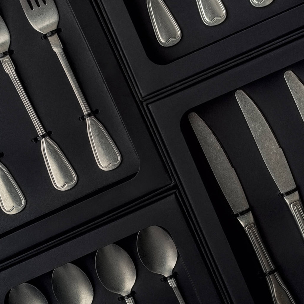 Top view of silver collection of knives, forks, spoons, tablespoons and teaspoons in black boxes on gray concrete background - Fotó, kép