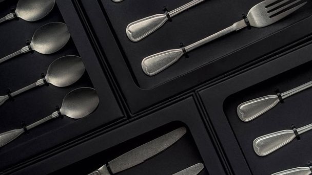 Top view of silver collection of knives, forks, spoons, tablespoons and teaspoons in black boxes on gray concrete background - Фото, изображение