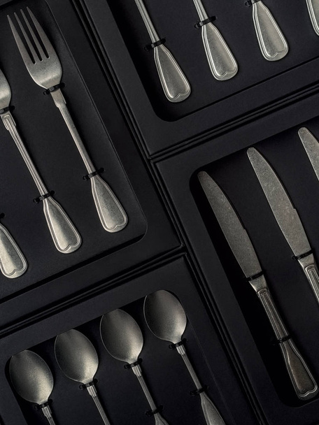 Top view of silver collection of knives, forks, spoons, tablespoons and teaspoons in black boxes on gray concrete background - 写真・画像