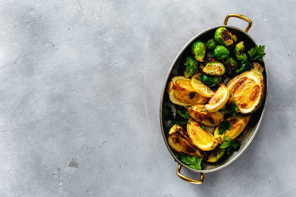 Vegetarian healthy dinner table concept. Fried brussels sprouts and zucchini served in frying pan on gray concrete background top view - Foto, imagen