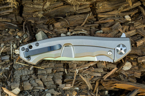 Messer mit Titangriff in gefalteter Form. Holz Hintergrund. - Foto, Bild