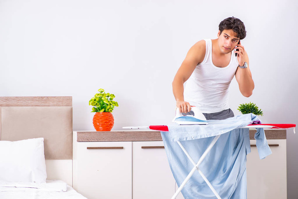 Young man ironing in the bedroom  - Fotó, kép