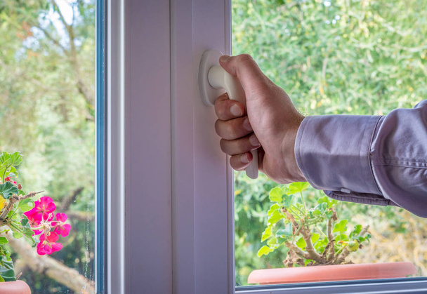 Mano masculina en la manija de una ventana blanca que mira al jardín
 - Foto, Imagen