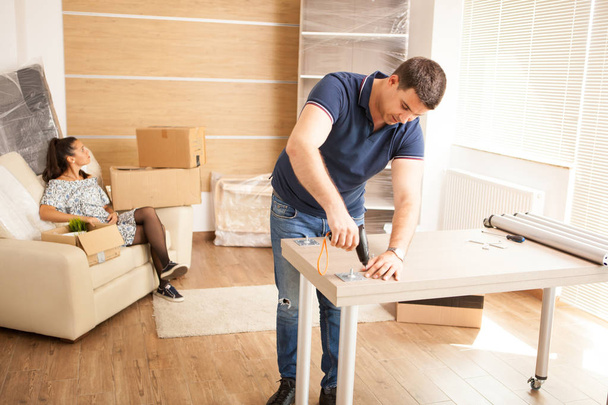 Улыбающийся человек собирает мебель для самосборки в новом доме
. - Фото, изображение