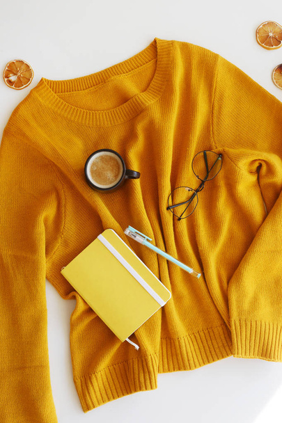 Jersey amarillo brillante con bloc de notas, bolígrafo, vasos y una taza de café. Humor y estilo otoñal. Vista superior, plano
 - Foto, imagen